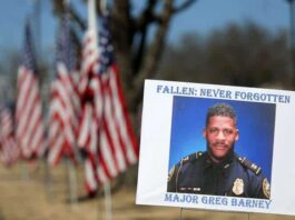A sign and flags honor Riverdale Police Maj. Greg Barney, who was not wearing a bulletproof vest when he was shot