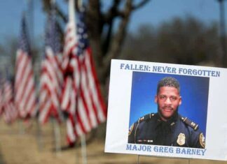 A sign and flags honor Riverdale Police Maj. Greg Barney, who was not wearing a bulletproof vest when he was shot