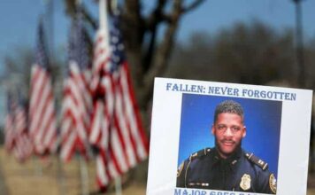 A sign and flags honor Riverdale Police Maj. Greg Barney, who was not wearing a bulletproof vest when he was shot