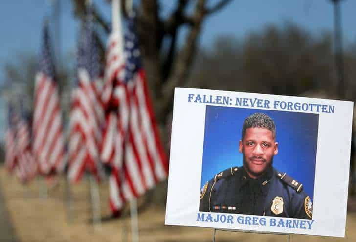 A sign and flags honor Riverdale Police Maj. Greg Barney, who was not wearing a bulletproof vest when he was shot